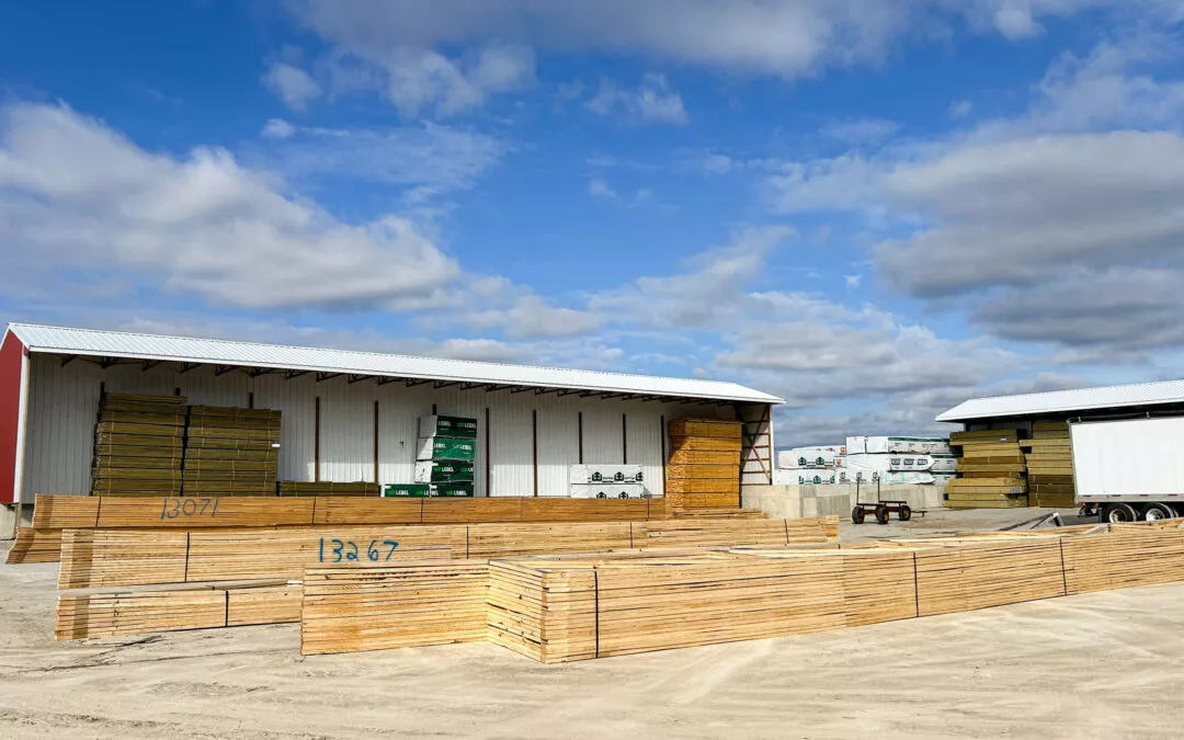 Martin's Truss Manufacturing Elkhart IN A large warehouse storing neatly stacked lumber in an open yard under a blue sky with clouds.