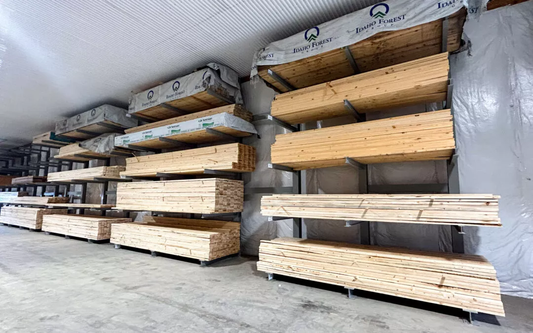 Martin's Truss Manufacturing Elkhart IN Stacks of lumber organized on shelving in a warehouse, each labeled with "pure forest" and protected with plastic sheeting.