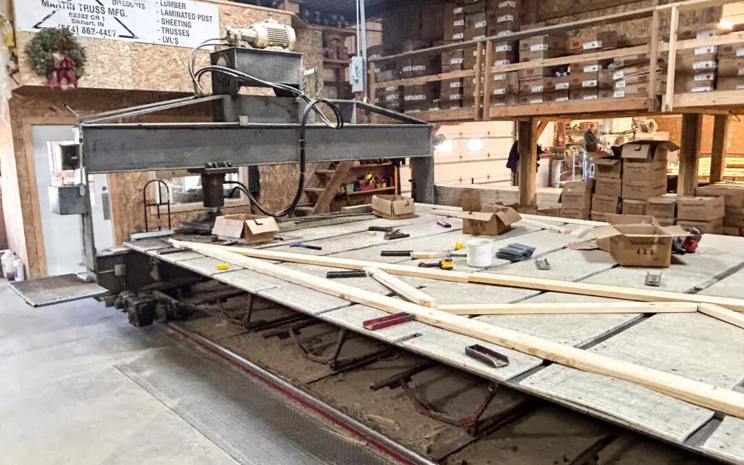 Martin's Truss Manufacturing Elkhart IN Interior of a cluttered woodworking shop with tools, wood planks on a large worktable, and storage shelves in the background.