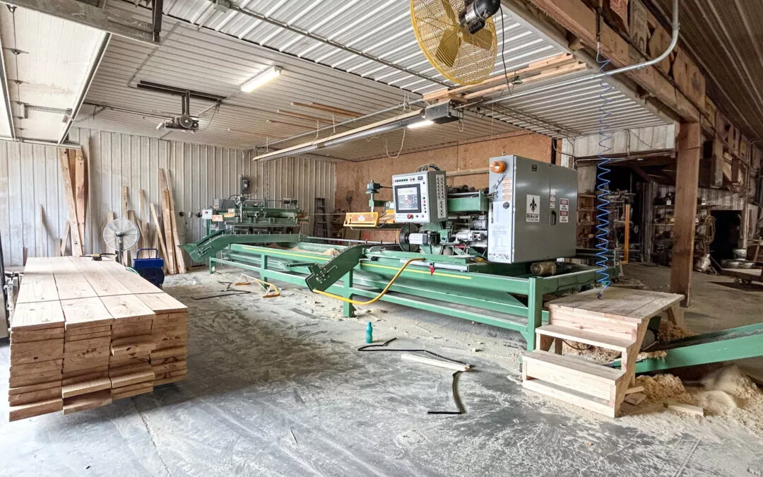 Martin's Truss Manufacturing Elkhart IN Interior of a woodworking workshop with various machines, sawdust on the floor, and a stack of wooden planks on the left.