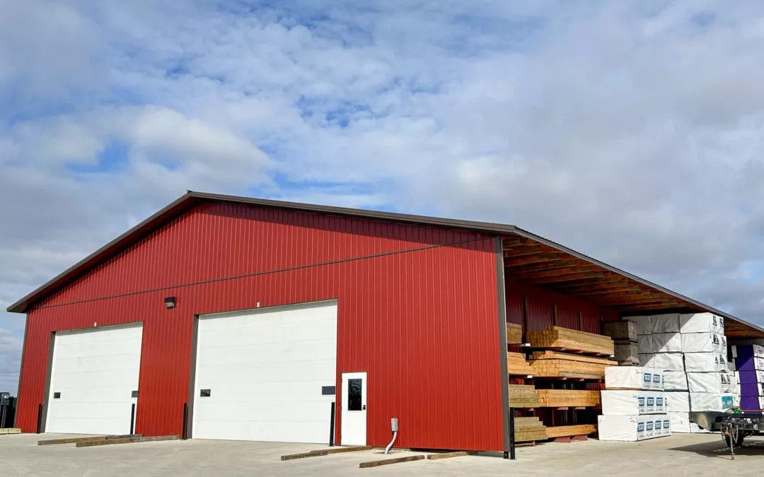 Martin's Truss Manufacturing Elkhart IN A large red warehouse with two white garage doors and a covered loading area with stacked materials under a blue sky.
