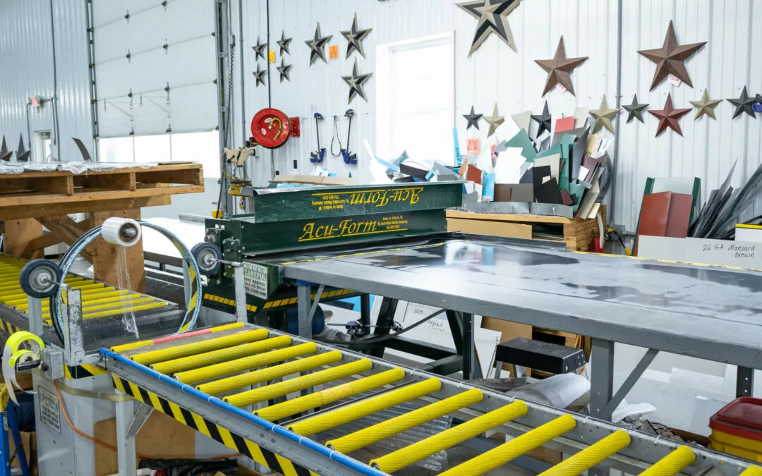 Martin's Trim Forming Millmont, PA A metal roofing trim manufacturing facility with a sheet metal bender, yellow roller conveyor, and various colored metal sheets and decorative stars on the walls.