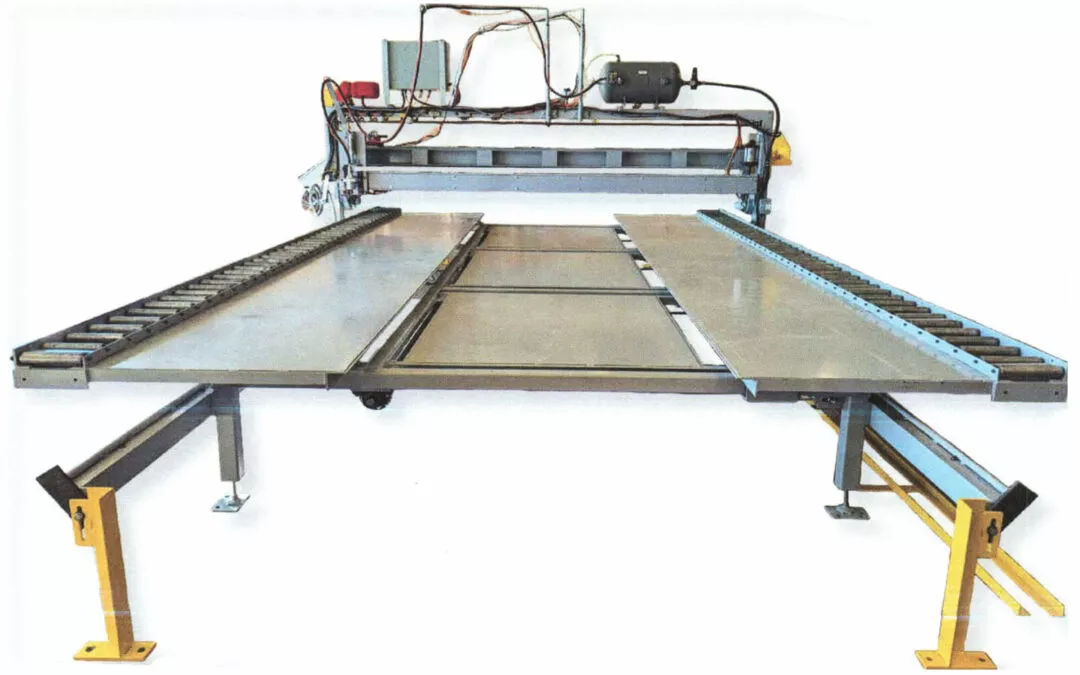Midstate Lamp LLC Arthur Illinois Industrial cutting machine with a large flat cutting bed, conveyor rollers on both sides, and electrical components mounted on top. The setup is supported by four yellow legs.