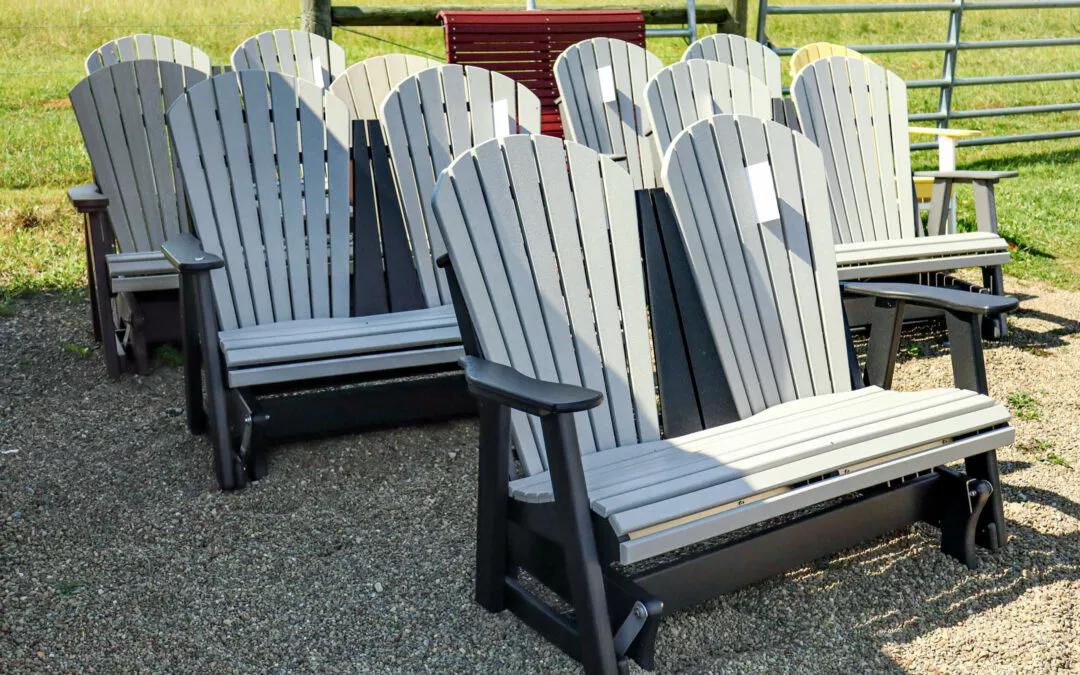 Summit Structures & Outdoor Living Greenville, PA Several white Adirondack-style benches with black bases arranged in rows on a gravel surface, set against a background of grass and a metal fence.