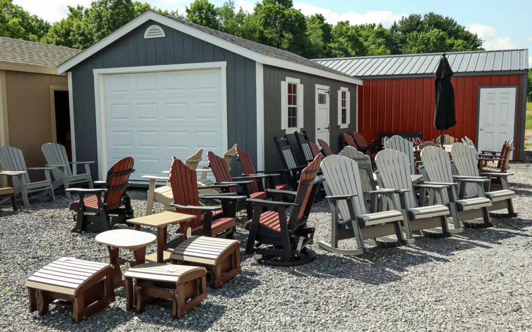 Summit Structures & Outdoor Living Greenville, PA Outdoor furniture store with various wooden chairs and tables displayed in front of a gray shed and a red building on a sunny day.