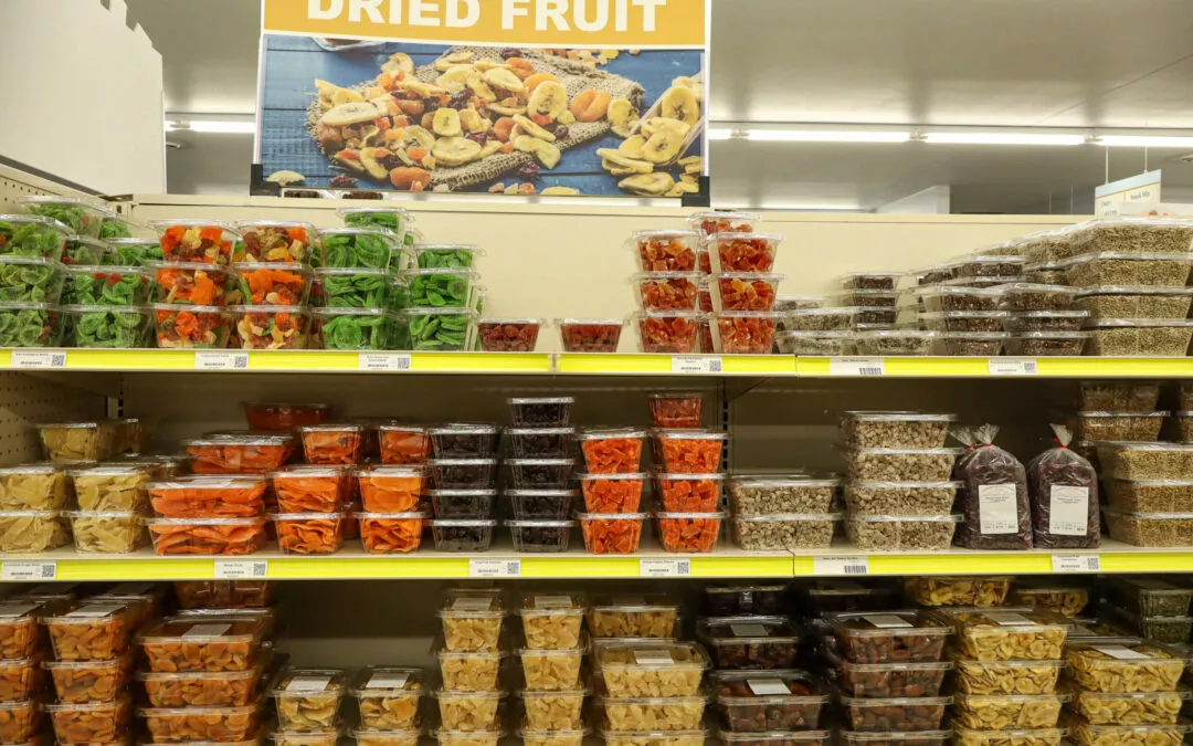 Lakeside Country Store Mishicot, Wisconsin A supermarket aisle filled with various plastic containers of dried fruit on shelves, labeled under a sign that reads "Dried Fruit." The selection includes multiple colors and types of dried fruit.
