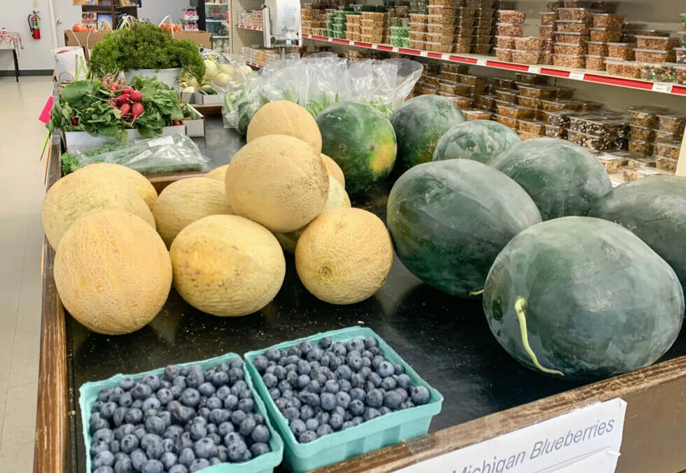 Lakeside Country Store Mishicot, Wisconsin A variety of fresh produce including melons, blueberries, and greens displayed on a market table with other items on shelves in the background.