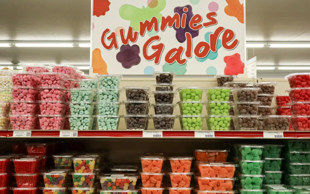 Lakeside Country Store Mishicot, Wisconsin A store shelf displays various colors and shapes of gummy candies in clear plastic containers under a sign reading "Gummies Galore.