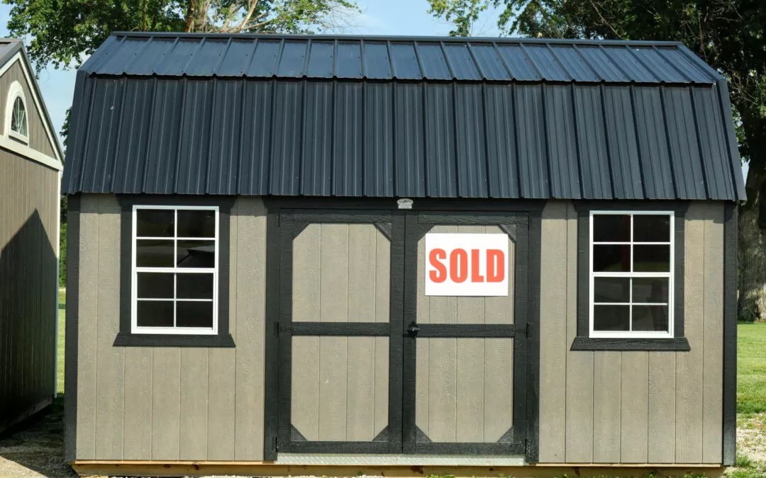 Cedar Ridge Sales Ramsey IL Ava IL A gray shed with a black roof and black trim, featuring a "SOLD" sign on its double doors. Two windows are visible, one on each side of the doors.