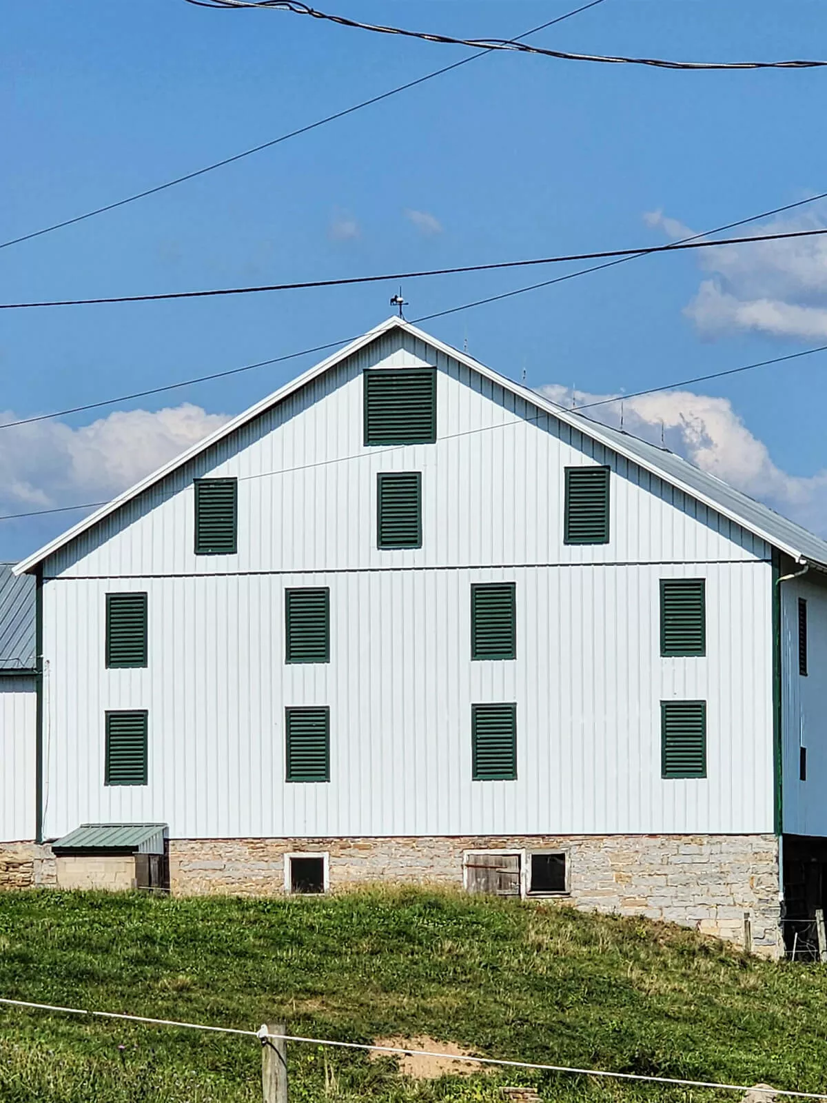 PREMEX Metal Roofing, Siding, & Trim Mifflinburg, PA A white barn with a metal roof stands on a grassy hill under a clear blue sky.