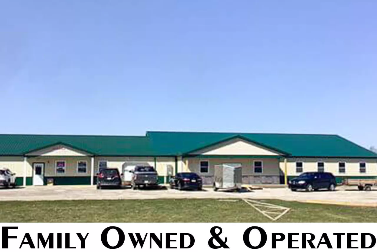 Blooming Grove Sewing Shiloh, OH A single-story building with a green roof and beige exterior. Several vehicles are parked in front. Large text below reads "Family Owned & Operated.