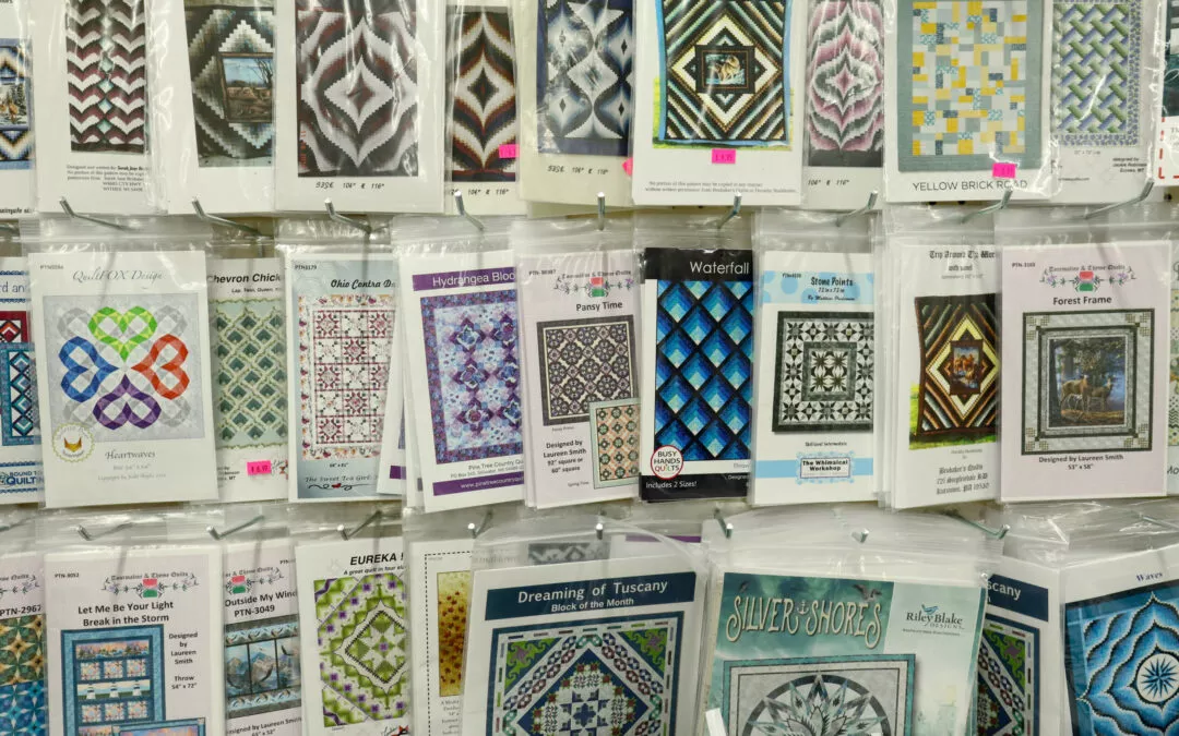 Brubaker's Sewing & Furniture Withee, WI A display of various quilt patterns in plastic packaging, featuring intricate geometric and floral designs in a range of colors.