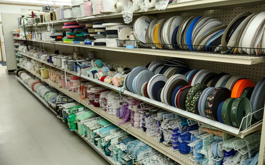 Brubaker's Sewing & Furniture Withee, WI Shelves stocked with various colorful ribbons and laces in a fabric store aisle.