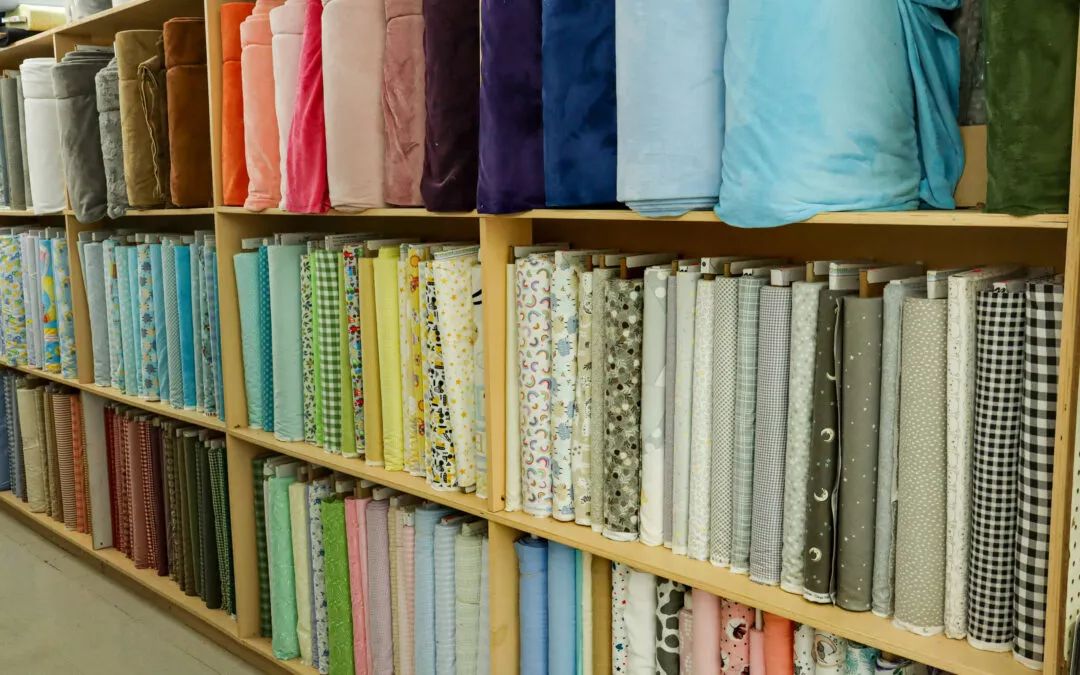 Brubaker's Sewing & Furniture Withee, WI Shelves filled with various rolls of fabric organized by color and pattern.
