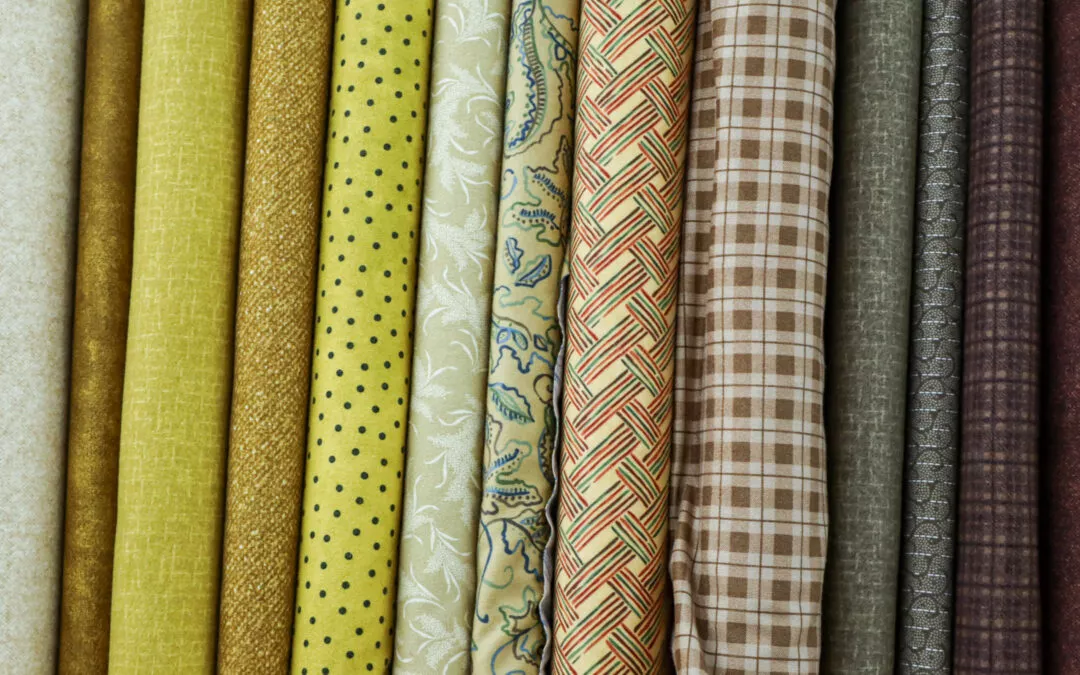 Brubaker's Sewing & Furniture Withee, WI A close-up of assorted rolls of fabric, each with differing patterns and colors, including polka dots, floral designs, and various plaid and textured prints.