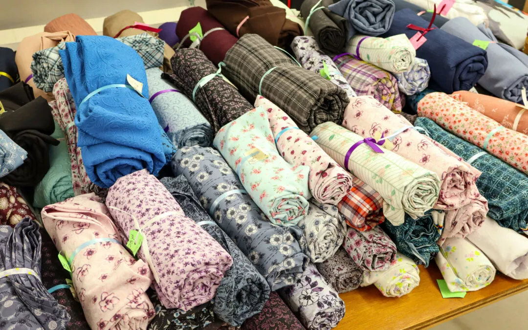 Brubaker's Sewing & Furniture Withee, WI A variety of fabric rolls in different colors and patterns are neatly displayed on a wooden table.