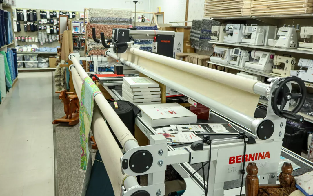 Brubaker's Sewing & Furniture Withee, WI A sewing store aisle with long-arm quilting machines, fabric rolls, stacked boxes, and shelves of sewing supplies and machines.