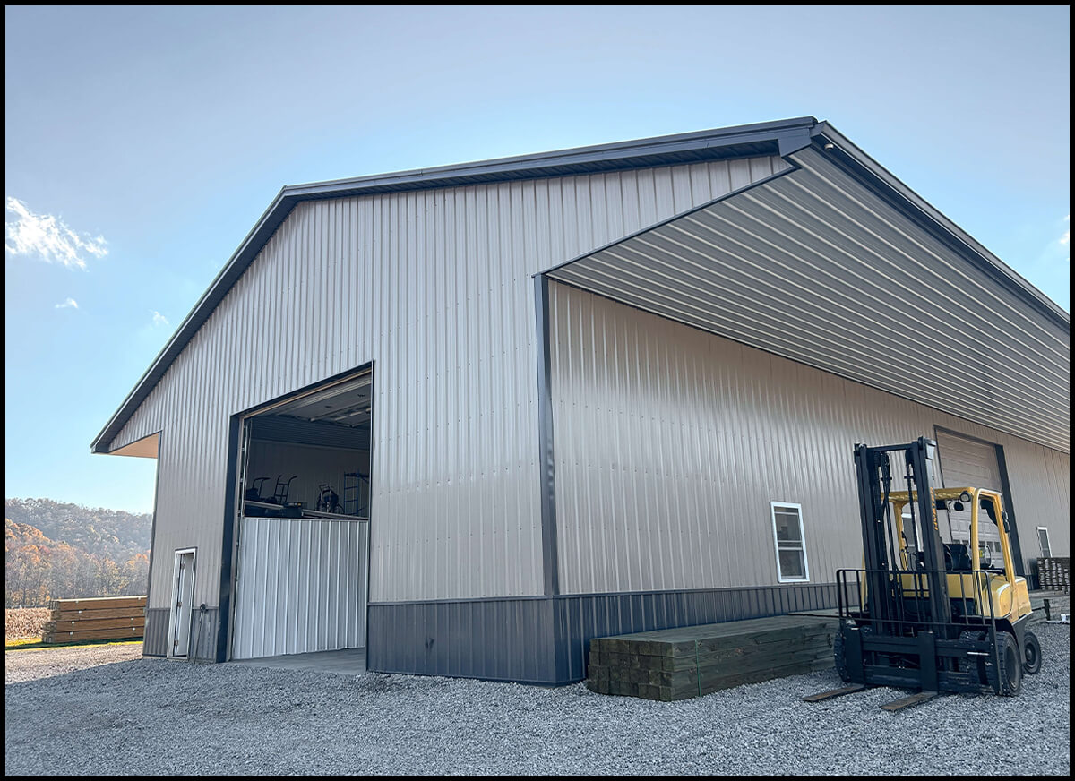 J and C Building Supplies Londonderry, OH A large metal warehouse with two tall open doors, housing a forklift inside. A yellow forklift is parked outside on a gravel lot under a clear sky.