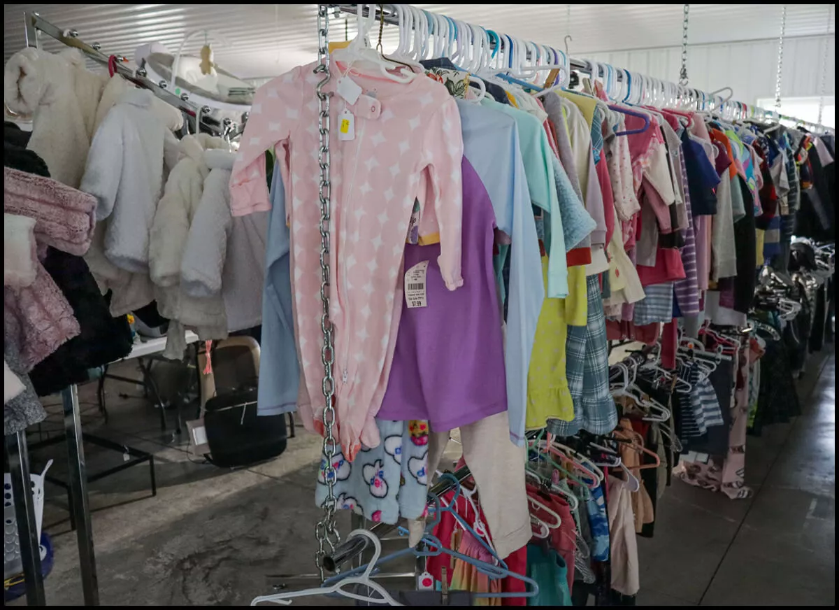 Secondhand Blessings Middlefield, OH Racks of children's clothing on hangers, including a pink star-patterned onesie, displayed in a store.