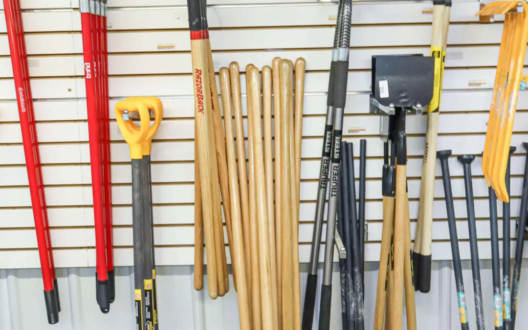 Chippewa Vallaey Dairy Supply Stanley, WI A variety of shovels and rakes with wooden and metal handles are displayed on a slatted wall in a store.