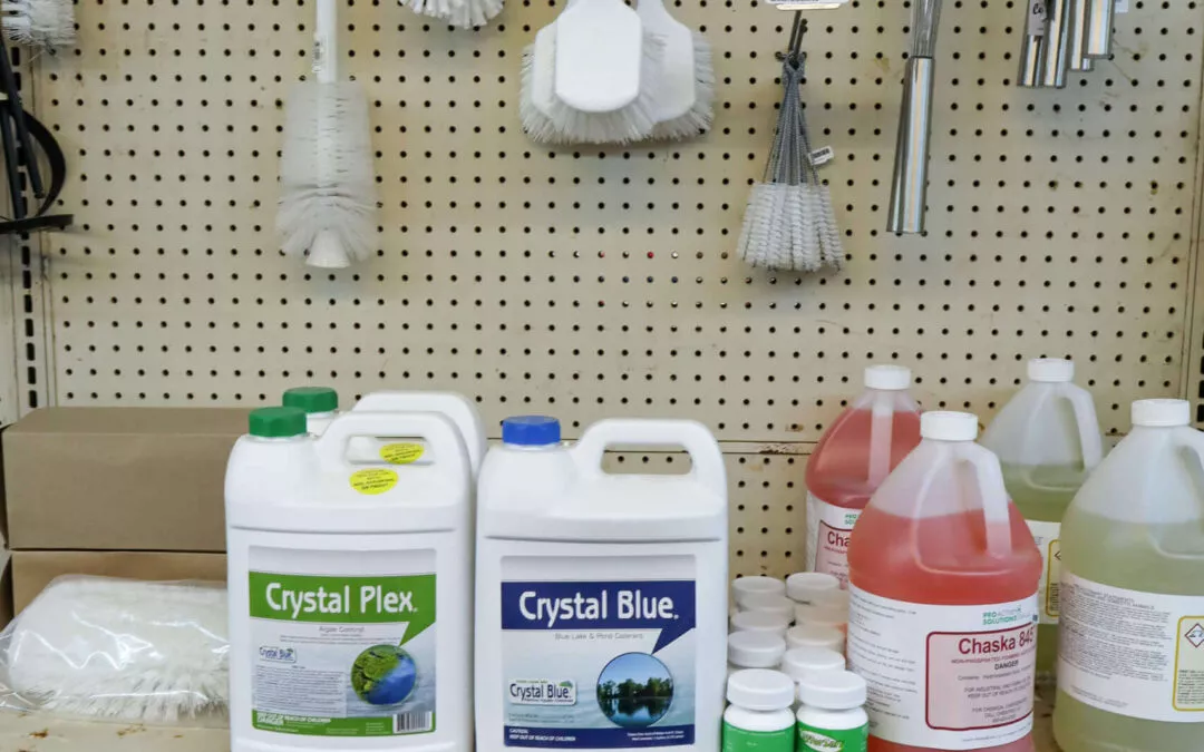 Chippewa Vallaey Dairy Supply Stanley, WI Cleaning and pool supplies displayed on shelves, including brushes, bottles labeled Crystal Plex and Crystal Blue, and large containers of chemicals.