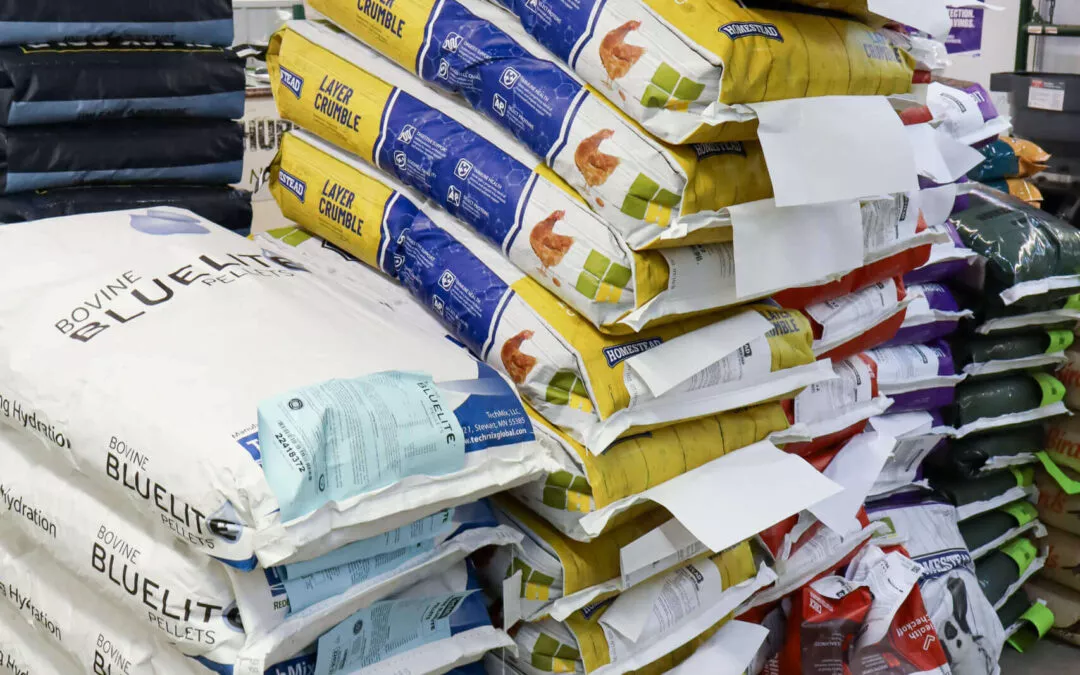 Chippewa Vallaey Dairy Supply Stanley, WI Stacks of animal feed bags in a store aisle, featuring various brands and colored packaging.