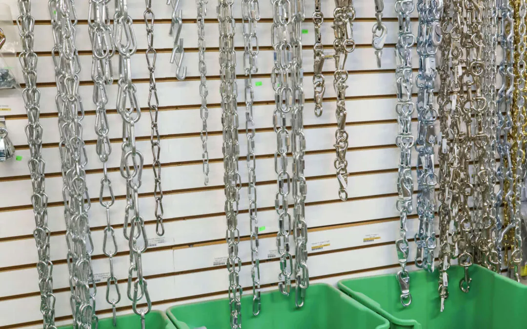 Chippewa Vallaey Dairy Supply Stanley, WI Various metal chains hang on a wall display above green bins filled with metal hardware in a store setting.