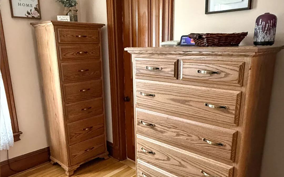 Sugar Valley Chair Shop Loganton, PA A room with two wooden dressers; one tall and narrow, the other wide. A framed picture and decorative items are on top. Light wood flooring and a window with a curtain are visible.
