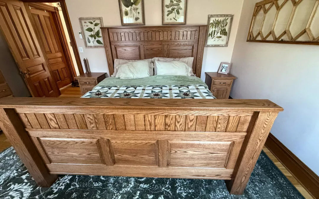 Sugar Valley Chair Shop Loganton, PA A bedroom with a wooden bed, green and white quilt, two nightstands, and botanical artwork on the walls. A mirror hangs on the right wall.