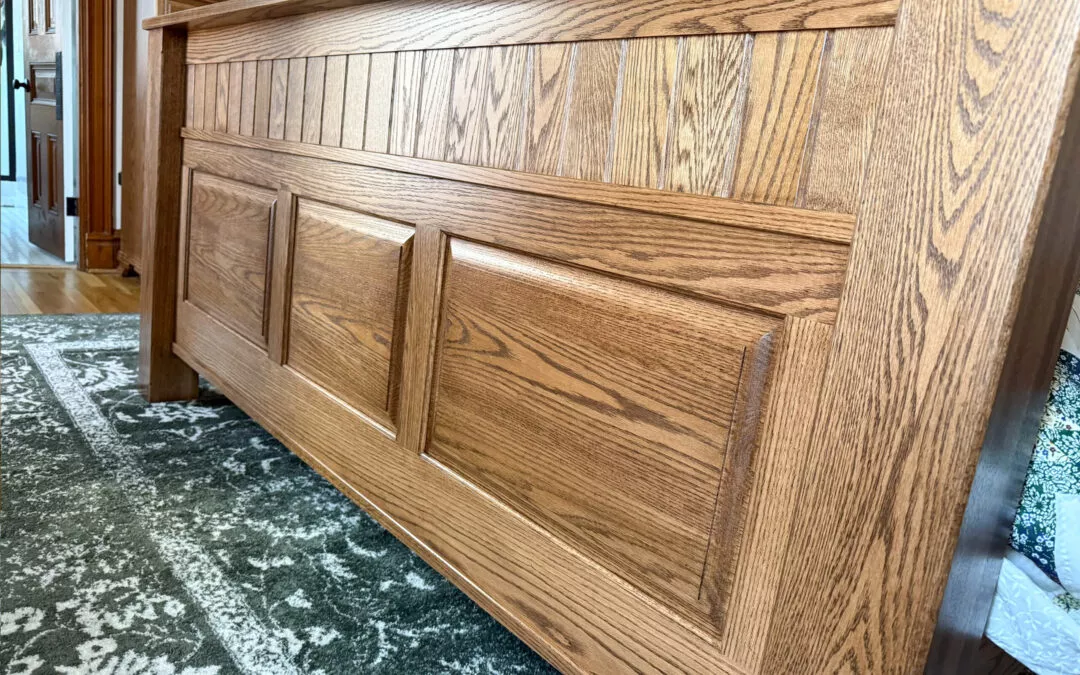 Sugar Valley Chair Shop Loganton, PA Wooden bed frame with vertical and horizontal paneling detail, set on a green patterned rug in a room.