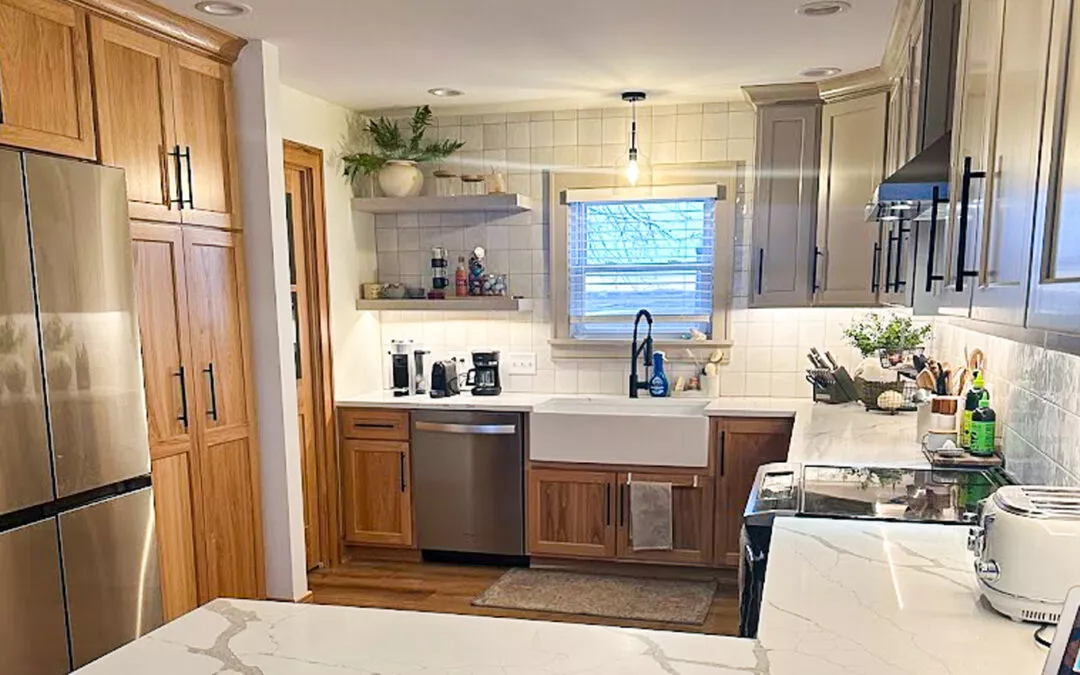 The Woodpecker Sullivan, Illinois Modern kitchen with wooden cabinets, marble countertops, stainless steel fridge and dishwasher, and a farmhouse sink under a window. Shelves hold plants and kitchen items.