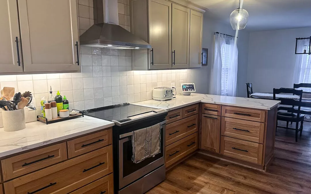 The Woodpecker Sullivan, Illinois A modern kitchen with a stainless steel stove and range hood, beige and wooden cabinets, white countertops, and a small dining area with a round table and chairs in the background.