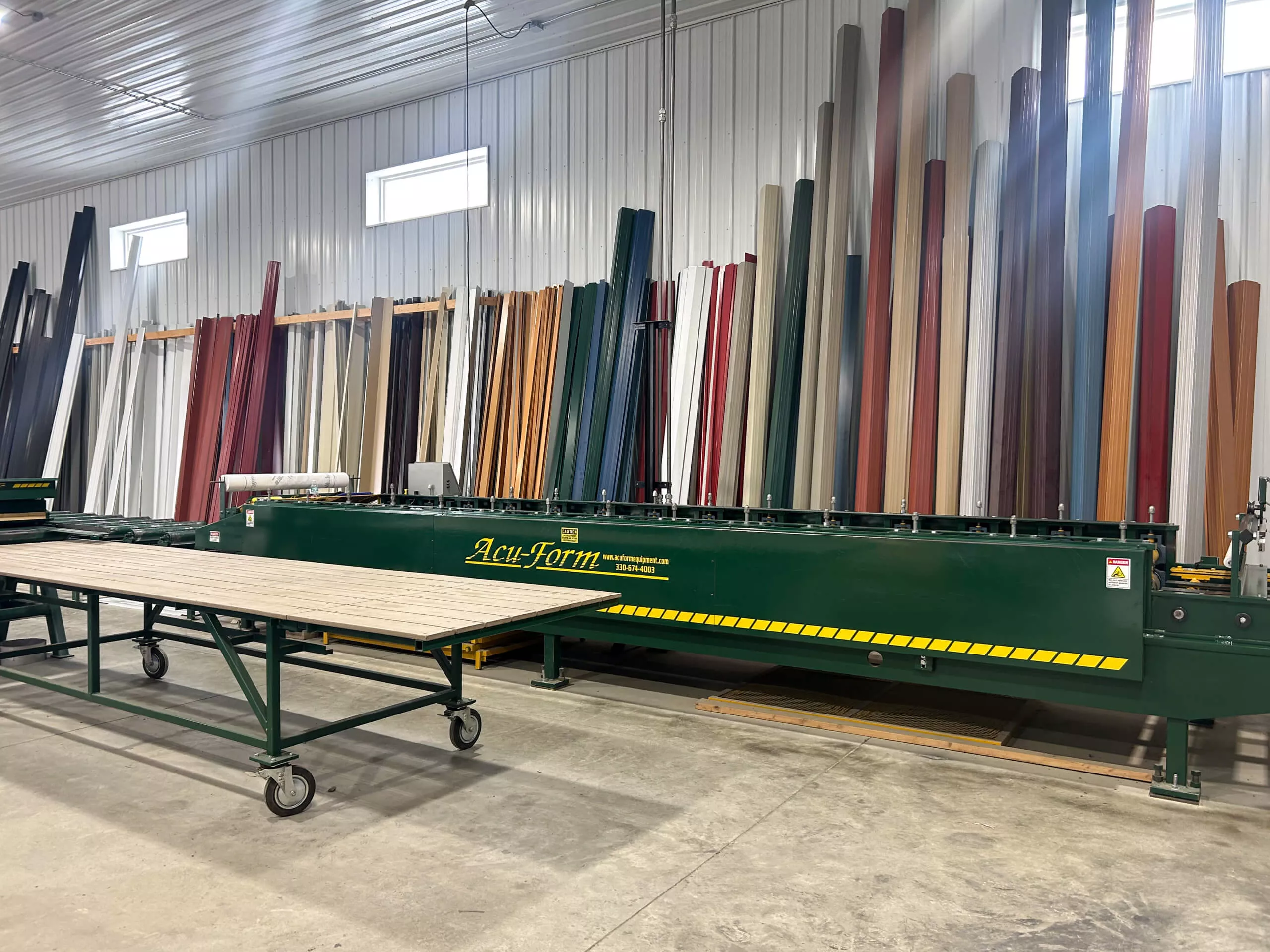 Amish Ridge Metals Perry, OH Large industrial metal bending machine labeled "Acu-Form" in a warehouse, with color metal sheet rolls stored vertically in the background.