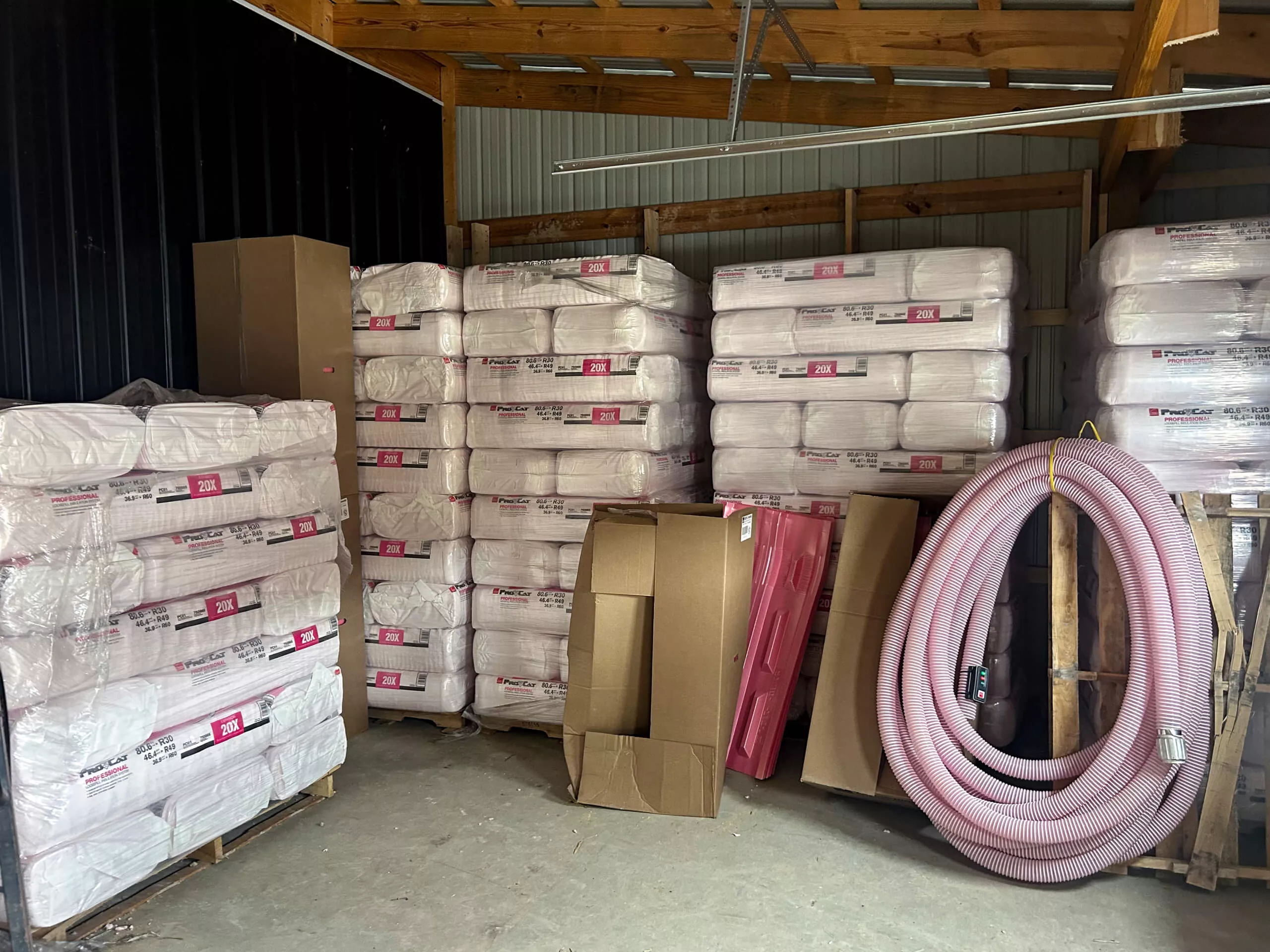 Amish Ridge Metals Perry, OH Stacks of insulation material wrapped in plastic are stored in a warehouse along with cardboard boxes, a large coiled hose, and other construction supplies.