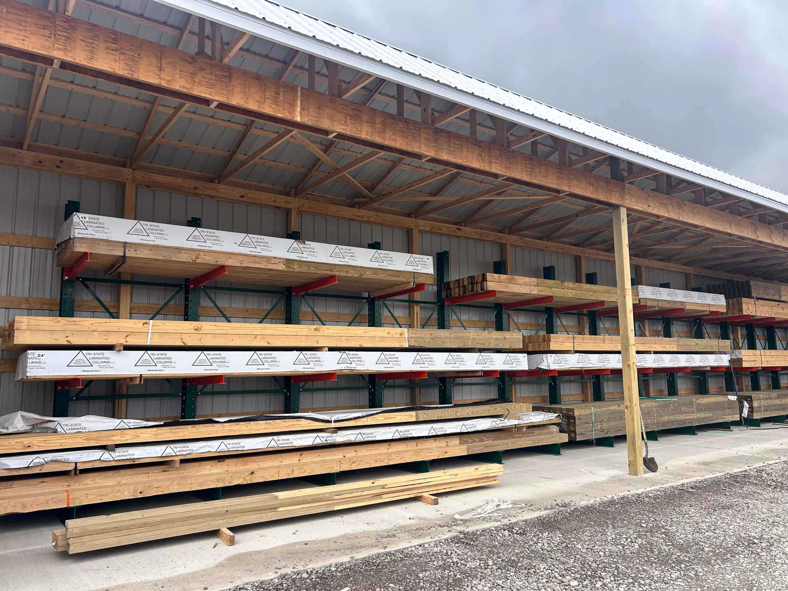 Amish Ridge Metals Perry, OH Stacks of lumber and building materials organized on metal shelves under a covered outdoor storage area at a lumber yard.