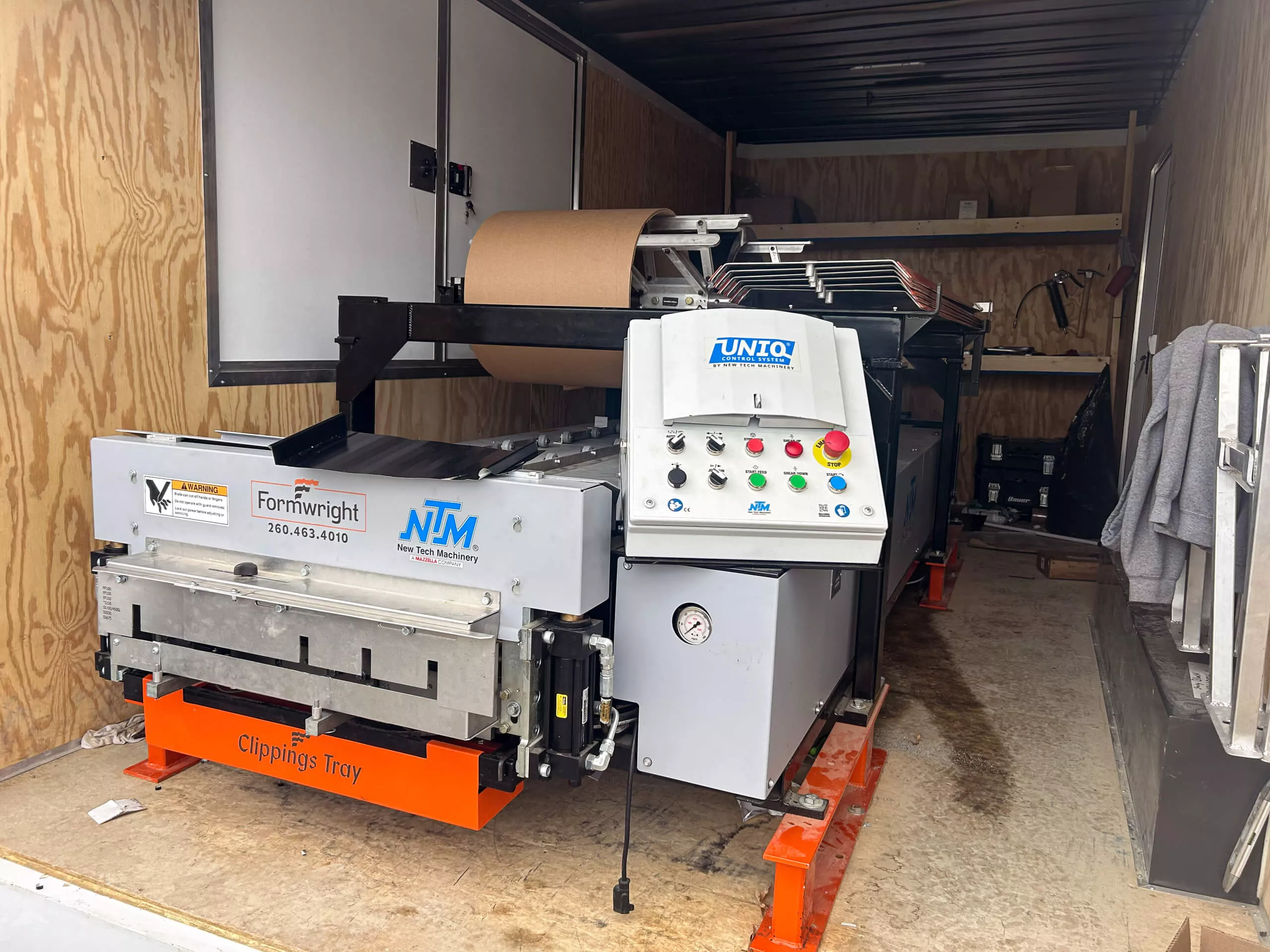 Amish Ridge Metals Perry, OH Industrial forming and wrapping machine inside a wooden trailer, with control panel, conveyor belt, and labeled clippings tray visible.