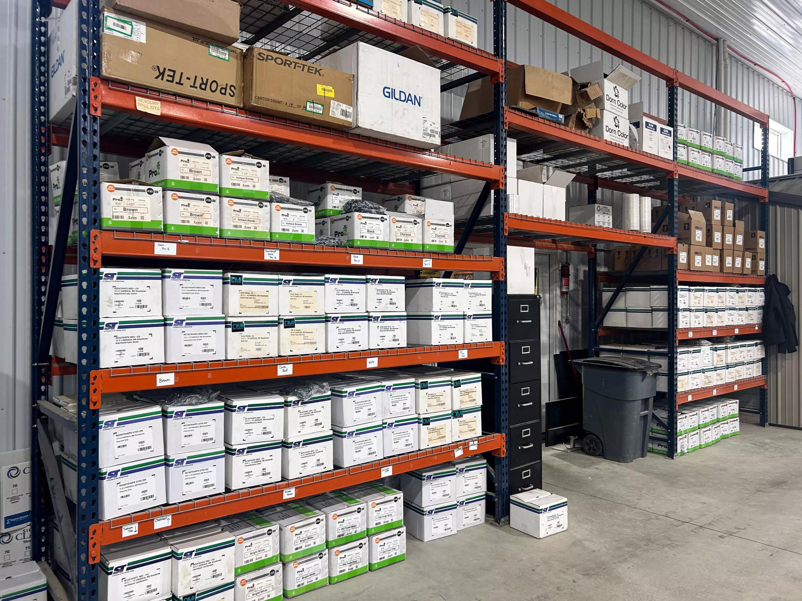 Amish Ridge Metals Perry, OH Metal shelves in a warehouse hold rows of labeled storage boxes and cardboard cartons. A filing cabinet, trash can, and coat are also visible in the organized space.