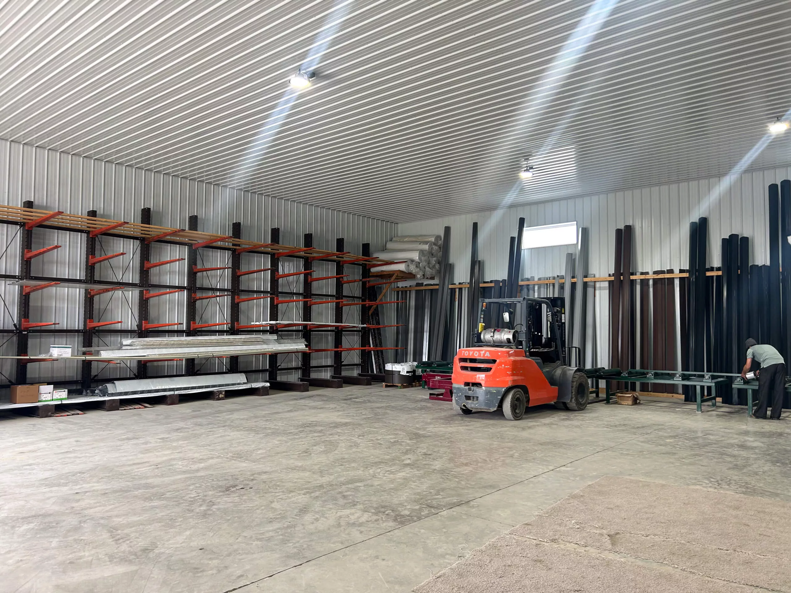 Amish Ridge Metals Perry, OH A forklift and a worker are in a spacious warehouse with metal shelves holding long pipes and materials against the walls.