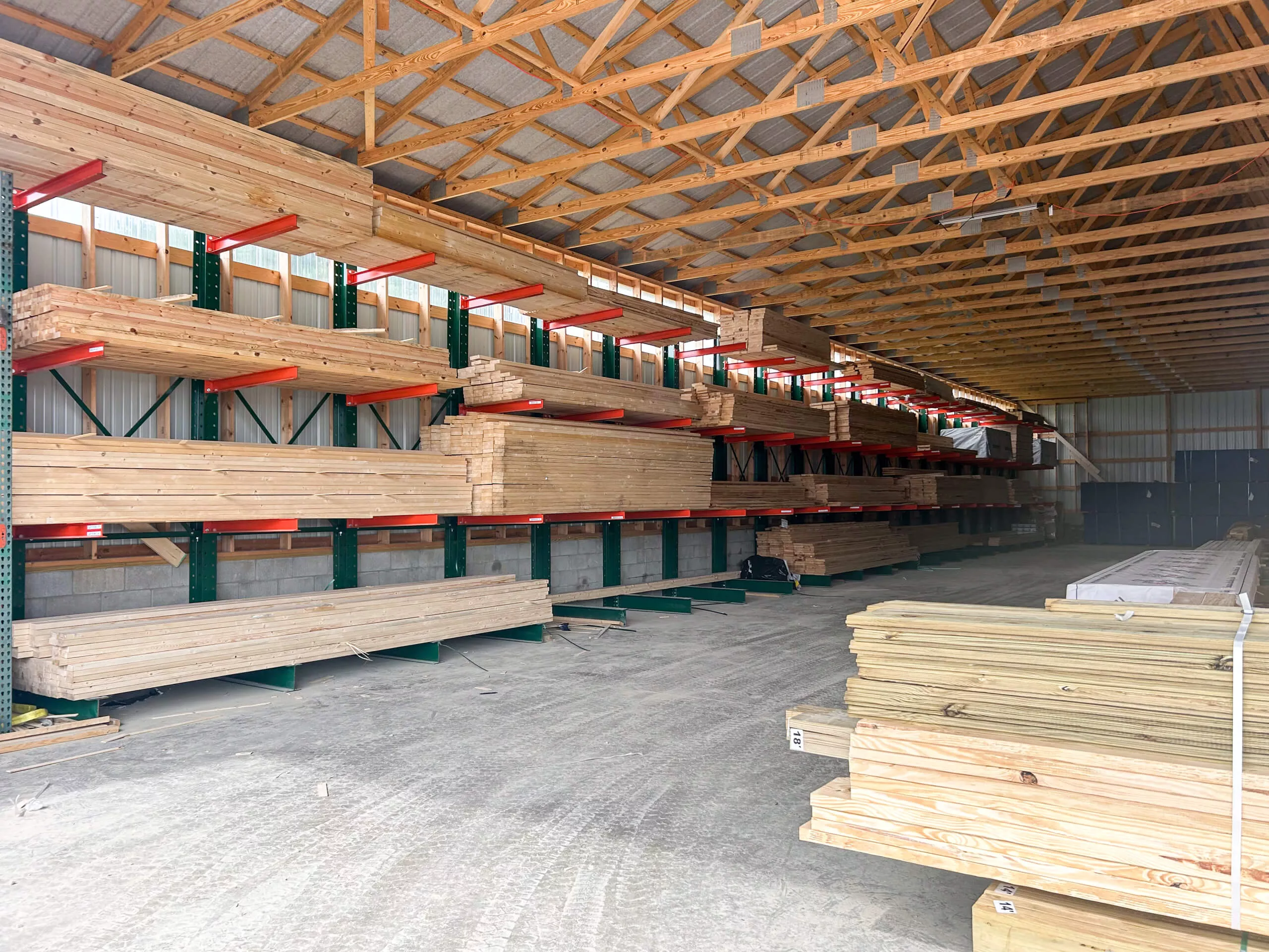 Amish Ridge Metals Perry, OH Stacks of lumber are organized on shelves inside a large, open warehouse with a wooden roof and concrete floor.
