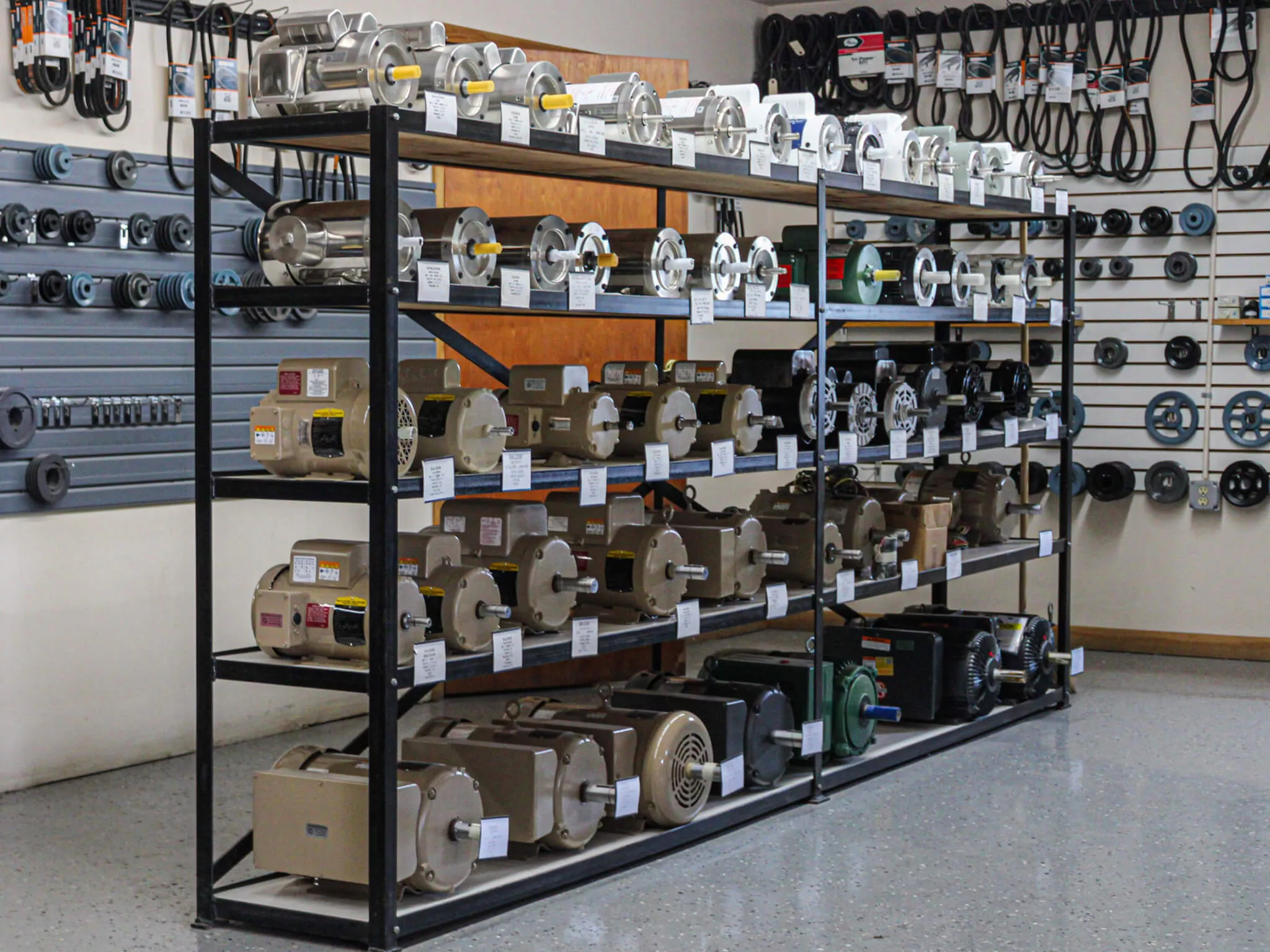 Shelves in a store display rows of electric motors, with various belts and pulleys hanging on the walls in the background.