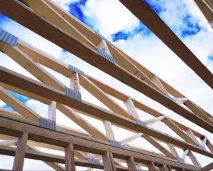 Wooden roof trusses under construction against a blue sky with clouds.