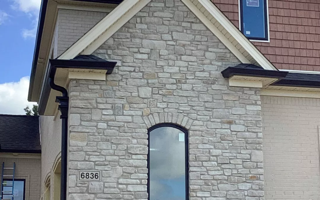 Miller's Guttering Seamless Gutters Arthur, IL A section of a house exterior with stone veneer, an arched window, and address number 6836. Part of a ladder is visible on the left side.