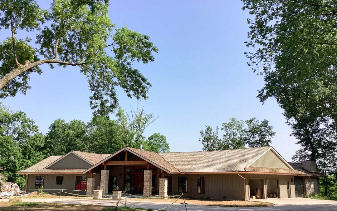 Miller's Guttering Seamless Gutters Arthur, IL A single-story house with a gabled roof, stone pillars, and a three-car garage, surrounded by trees on a clear day.