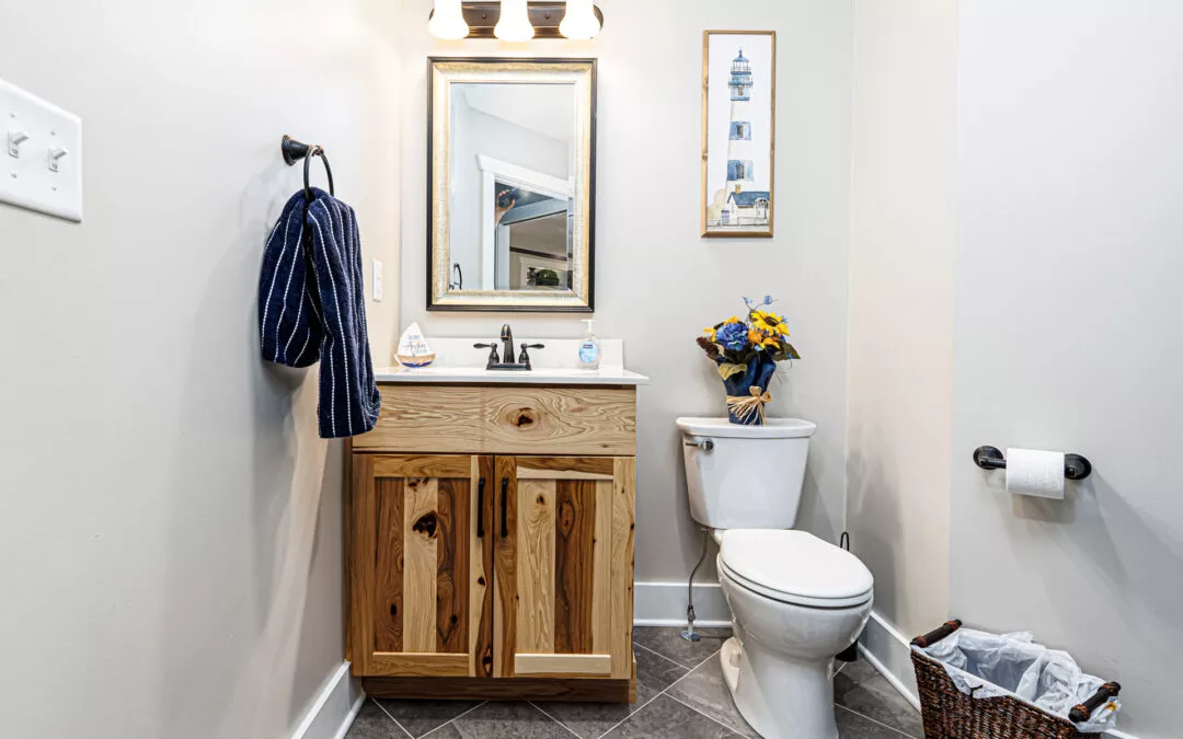 Noah F. Boyle Cabinets Elizabethtown, PA Small bathroom with wooden vanity, mirror, and light fixture above sink; toilet with a basket and a vase of flowers; towel on wall; lighthouse picture hanging on white wall.
