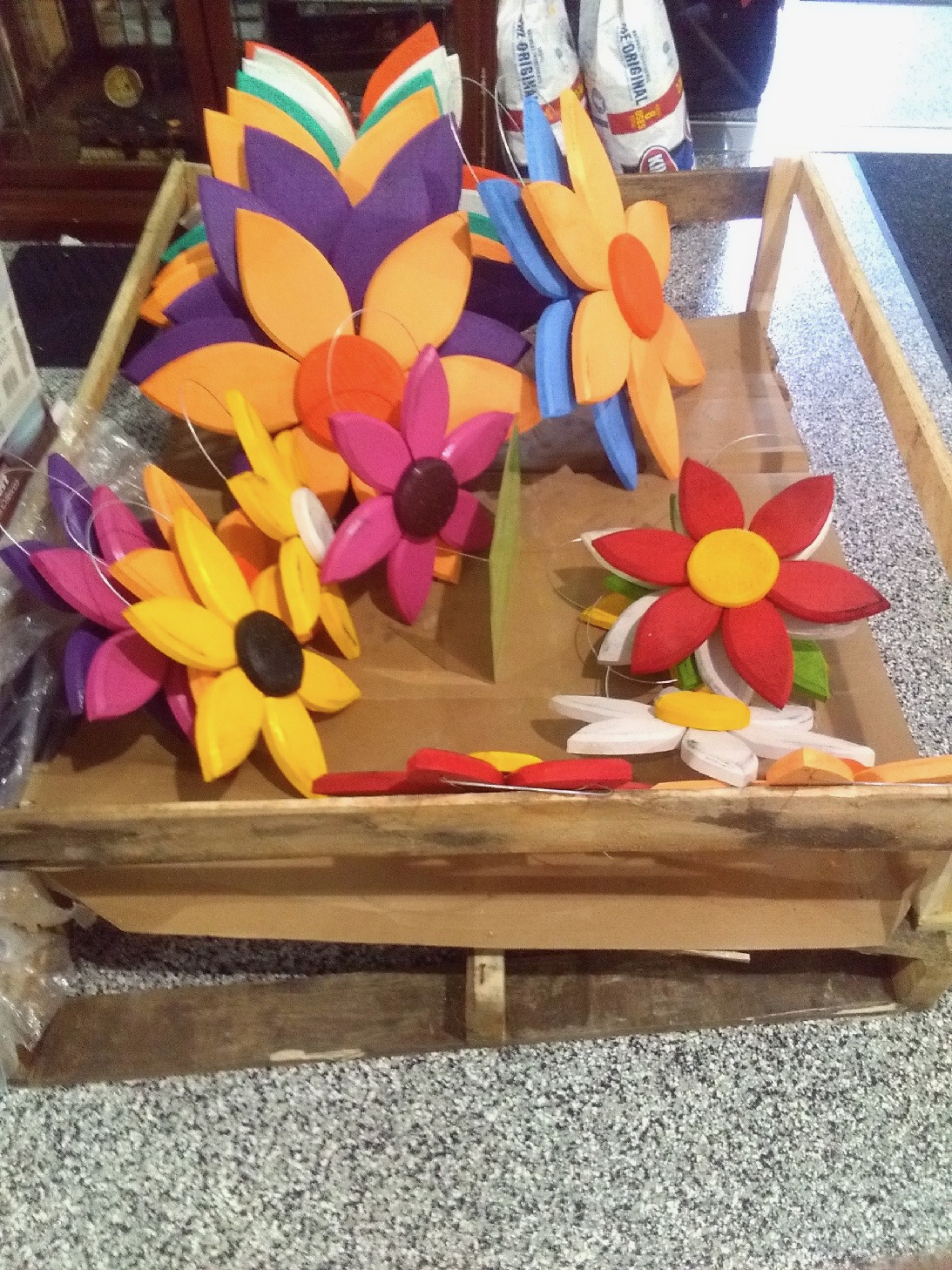 KIMG0051 A wooden crate on a speckled countertop filled with colorful, handcrafted wooden flowers in various shapes and sizes.