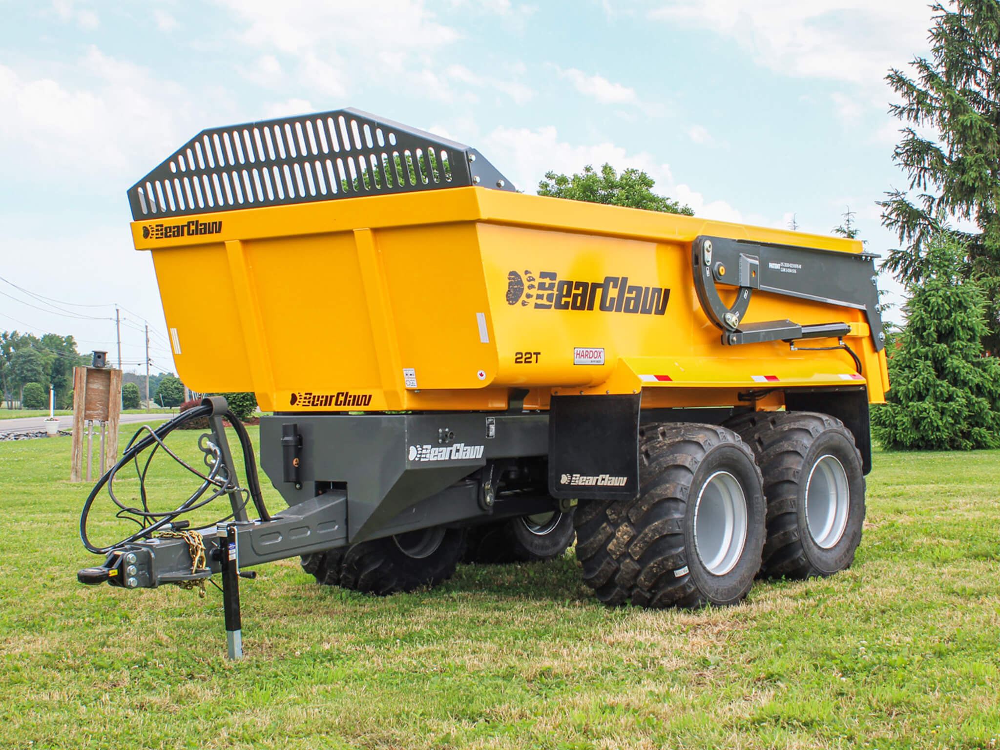 A large yellow BearClaw 22T dump trailer with six wheels is parked on grass under a partly cloudy sky.