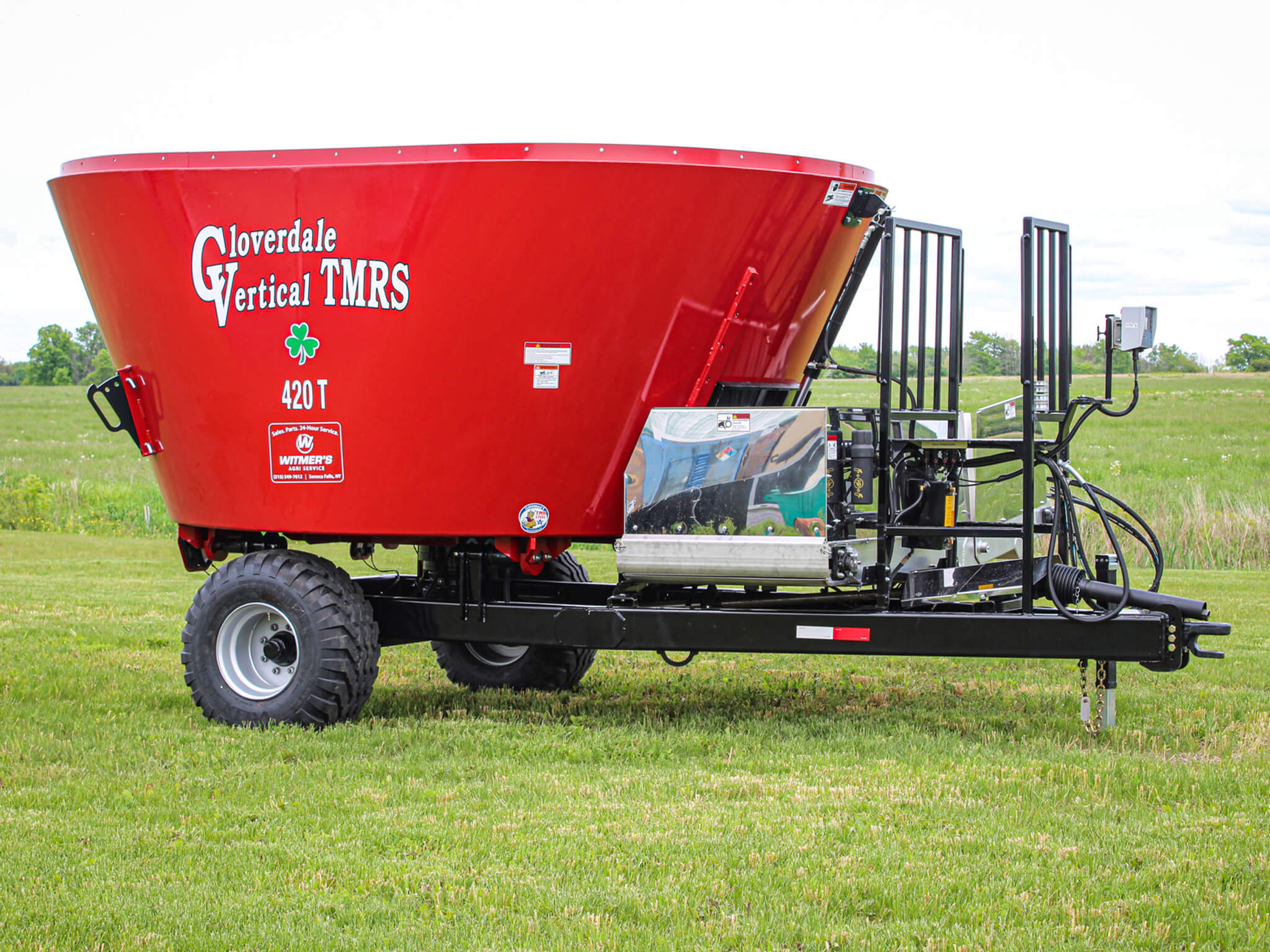 A red Cloverdale Vertical TMR 420T feed mixer is parked on a grassy field with a green landscape in the background.