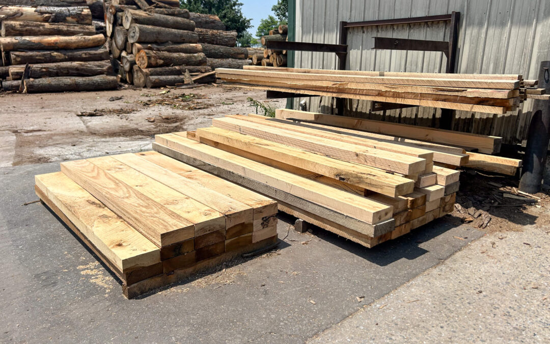 Leinbach's Sawmill Lumber Lancaster, PA Several stacks of cut lumber are piled on the ground and on racks outside near a metal building; logs are visible in the background.