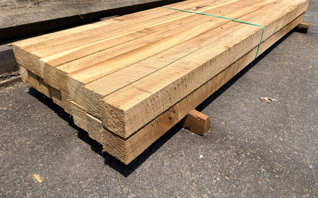 Leinbach's Sawmill Lumber Lancaster, PA A stack of rough-sawn wooden planks bound with a green strap rests on wooden blocks on a concrete surface.