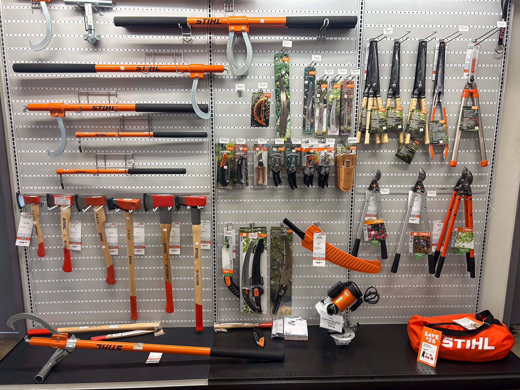 7.9.25 Martin's Small Engine Repair Arborist Photo Display of assorted gardening and cutting tools, including axes, loppers, pruning saws, and shears, arranged on a pegboard wall with STIHL branding and price tags visible.